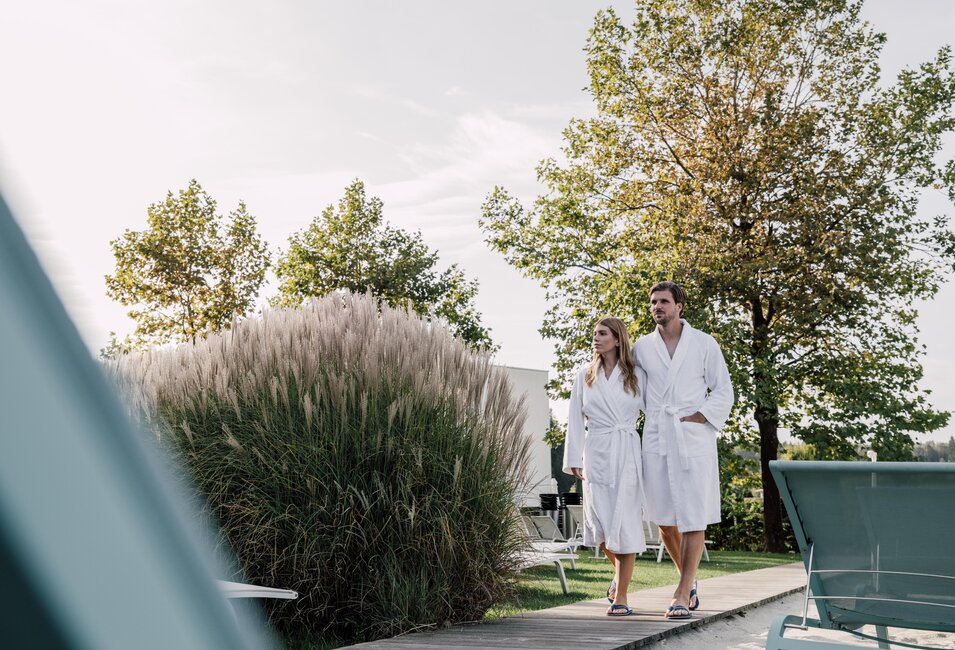 Paar im Bademantel geht durch den Strand-Liegebereich der Karibischen Saunawelt im Spa Resort Geinberg | © Spa Resort Geinberg / Chris Perkles