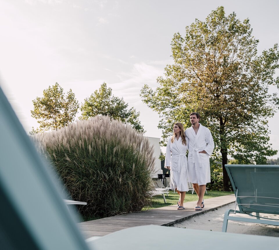 Paar im Bademantel geht durch den Strand-Liegebereich der Karibischen Saunawelt im Spa Resort Geinberg | © Spa Resort Geinberg / Chris Perkles