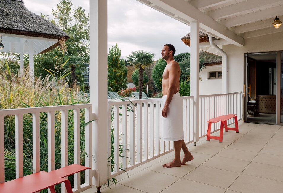 Mit Badetuch gekleideter Mann blickt auf die Karibische Saunawelt mit Strand und Palmen im Spa Resort Geinberg | © Spa Resort Geinberg / Chris Perkles