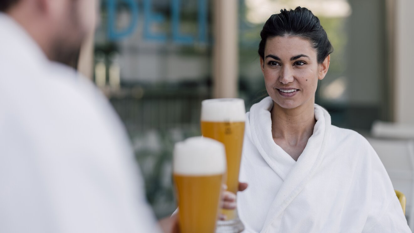 Paar im Bademantel genießt ein kühles Bier im Sauna-Bistro des Spa Resort Geinberg | © Spa Resort Geinberg / Chris Perkles