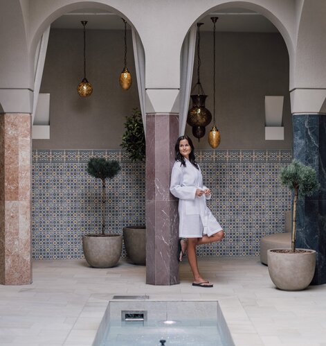 Entspannte Frau lehnt sich an eine Säule im Bademantel im SPAplus Arkadenhof | © Spa Resort Geinberg / Chris Perkles