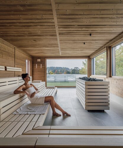 Frau entspannt in Holzsauna mit Panoramablick auf Landschaft | © Spa Resort Geinberg / Chris Perkles