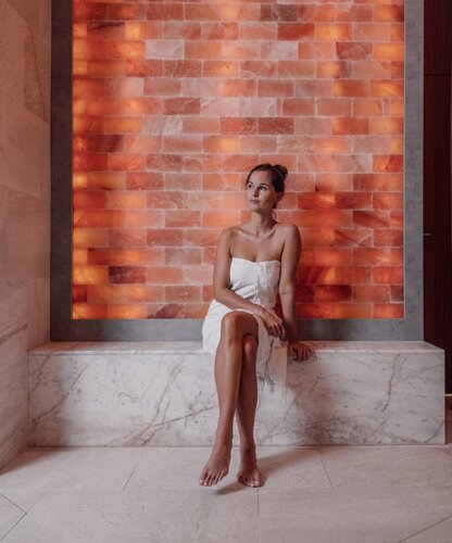 Junge Frau im Handtuch sitzt vor beleuchteter Salzwand | © Spa Resort Geinberg / Chris Perkles