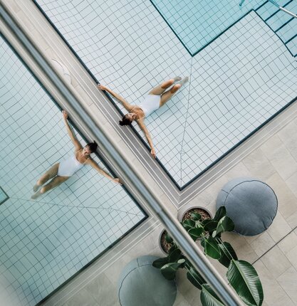 Gespiegeltes Bild einer Frau im weißen Badeanzug, die entspannt im Pool liegt und dadurch zweimal zu sehen ist | © Spa Resort Geinberg / Chris Perkles