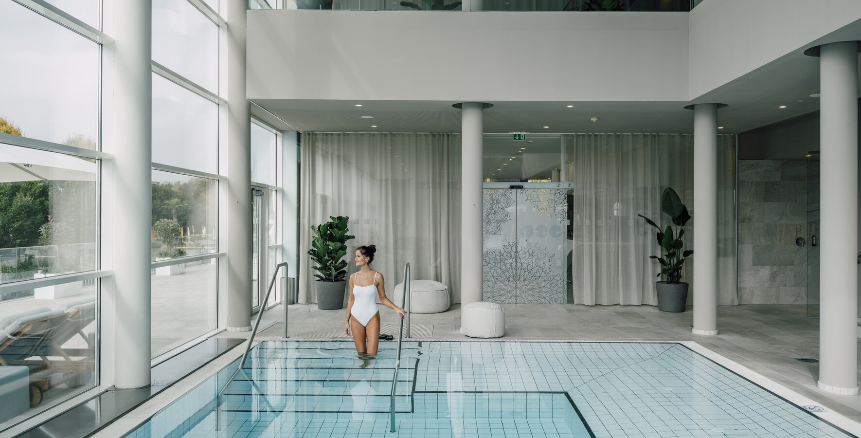 Frau im weißen Badeanzug steigt in hellen Hallenbad | © Spa Resort Geinberg / Chris Perkles