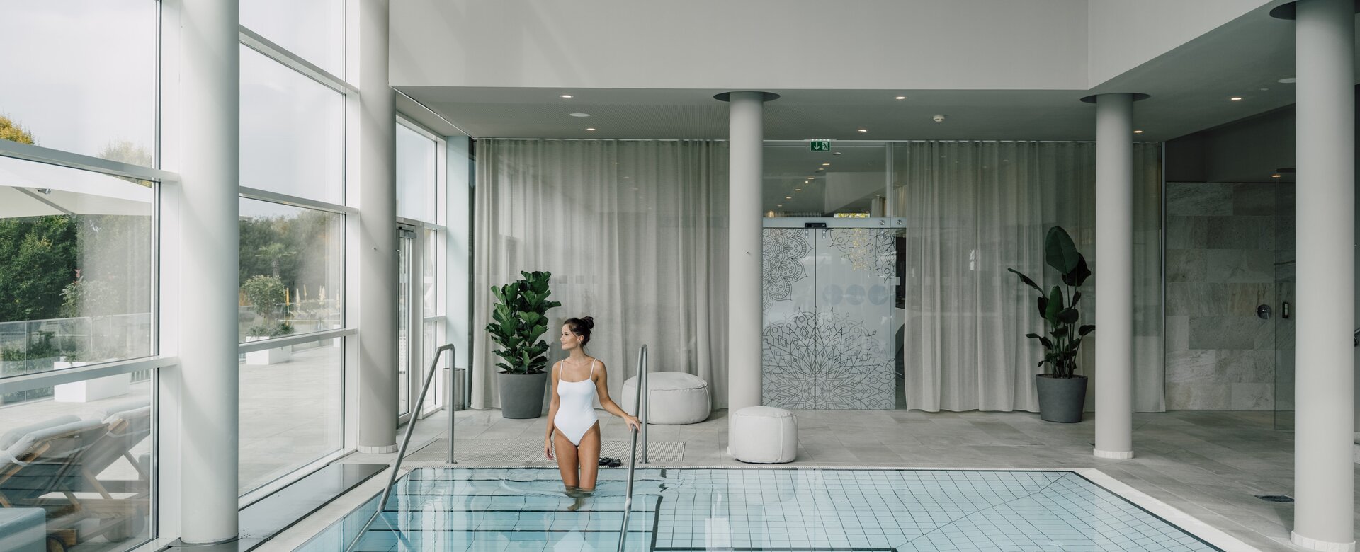 Frau im weißen Badeanzug steigt in hellen Hallenbad | © Spa Resort Geinberg / Chris Perkles
