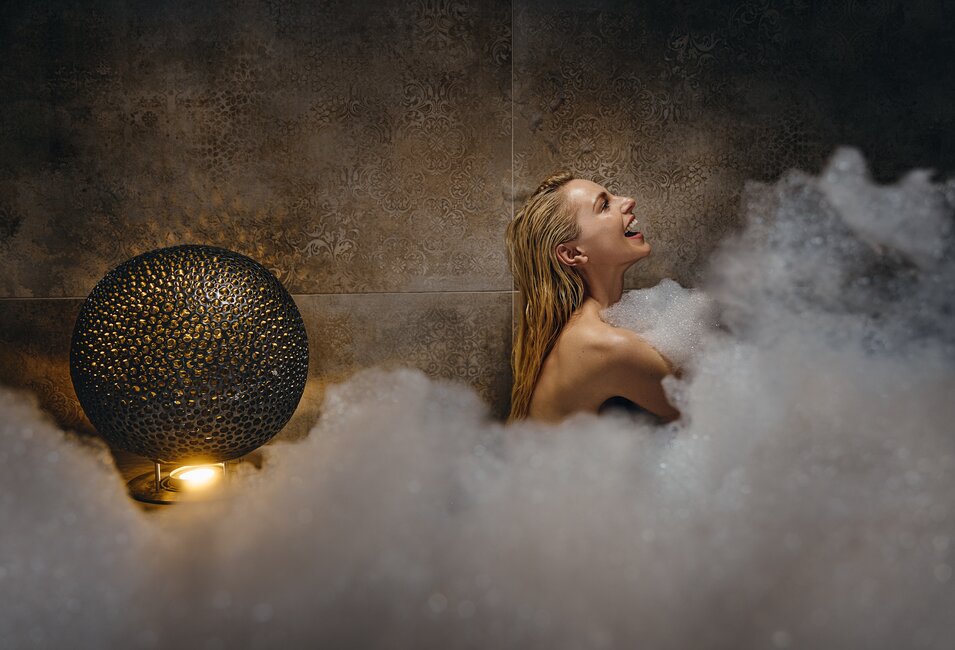 Lachende Frau in luxuriösem Schaum-Dampfbad