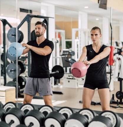Paar trainiert mit Kettlebells im Fitnesscenter vor Spiegelwand