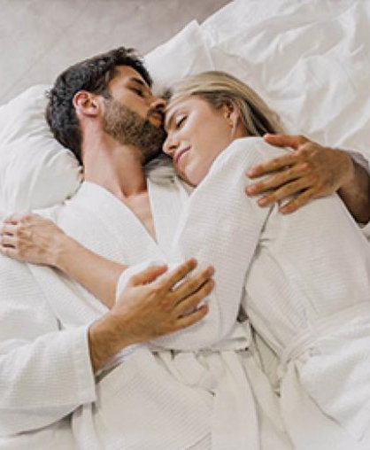 Zärtlich umarmendes Paar in weißen Bademänteln im Bett