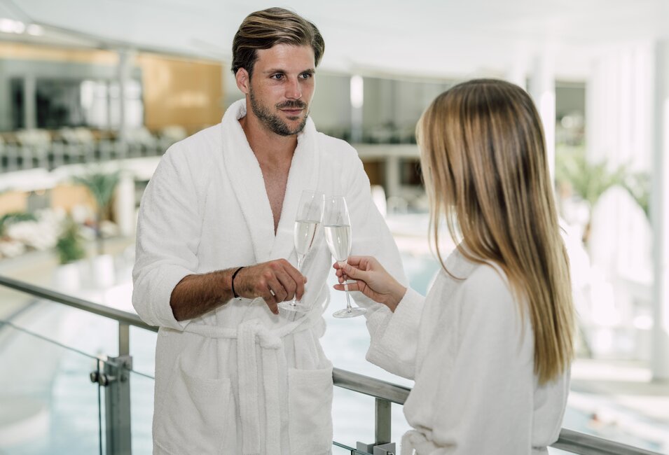 Paar im Bademantel stößt mit zwei Gläsern Prosecco in der Therme des Spa Resort Geinberg an | © Spa Resort Geinberg / Chris Perkles