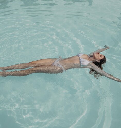 Blonde Frau in weißem Bikini schwebt im Wasser der Karibik-Lagune im Spa Resort Geinberg | © Spa Resort Geinberg / Chris Perkles
