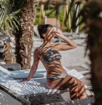 Frau im Bikini entspannt auf Liege am Strand unter Palmen in der Karibik Lagune | © Spa Resort Geinberg / Chris Perkles