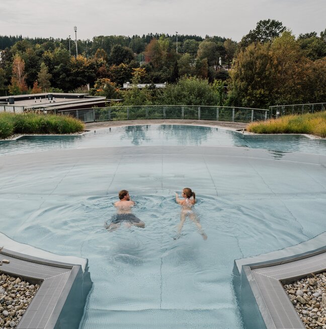 Paar schwimmt im Kaskaden-Becken des Spa Resort Geinberg mit Blick auf die Innviertler Umgebung | © Spa Resort Geinberg / Chris Perkles