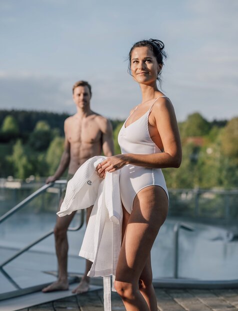 Frau im weißen Badeanzug mit Handtuch, Mann ohne Oberteil am Beckenrand | © Spa Resort Geinberg / Chris Perkles