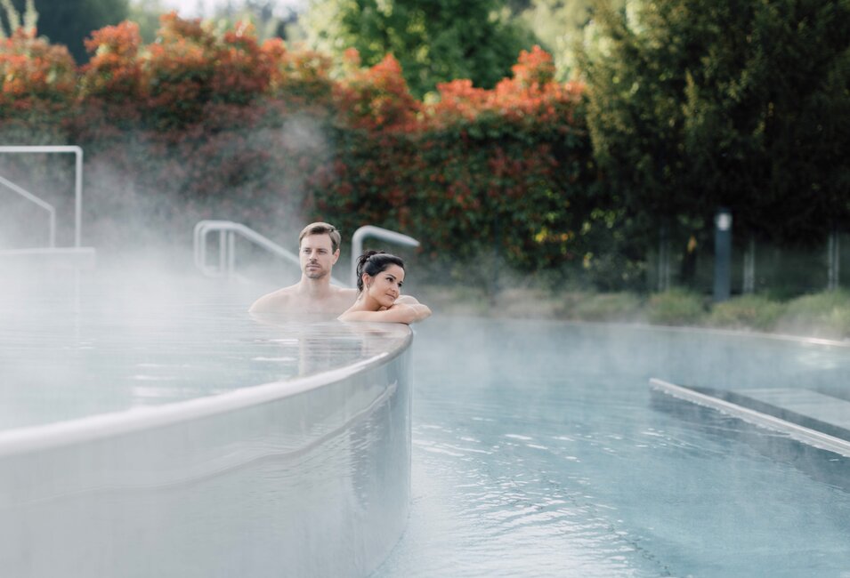 Paar im dampfenden Kaskadenbecken des Spa Resort Geinberg vor Bäumen | © Spa Resort Geinberg / Chris Perkles