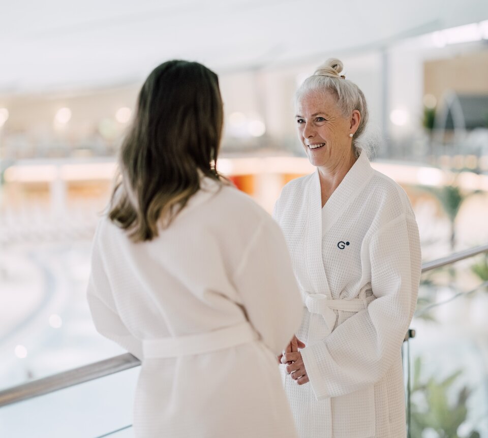 Mutter und Tochter im Bademantel unterhalten sich im hellen Innenbereich einer Therme | © Spa Resort Geinberg / Chris Perkles
