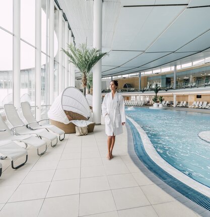 Frau im Bademantel geht an Thermalbecken mit Glasfront entlang | © Spa Resort Geinberg / Chris Perkles