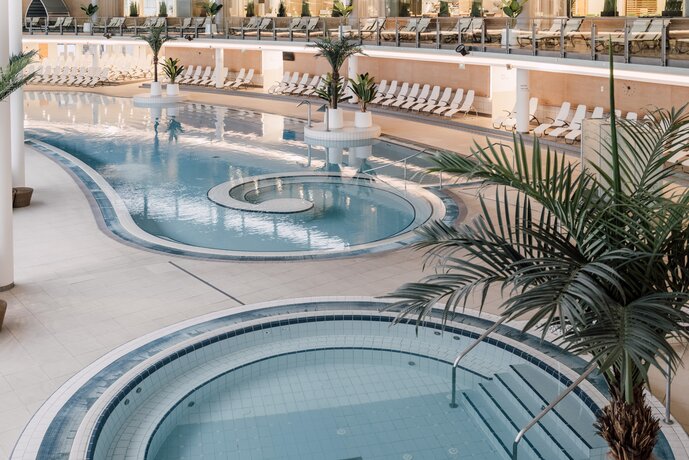 Thermal-Becken indoor - Vorne sehen Sie den Whirlpool im Innenbereich. Dahinter erstreckt sich das Thermal-Wasser-Becken mit der Möglichkeit nach draußen zu schwimmen.  | © Spa Resort Geinberg / Chris Perkles