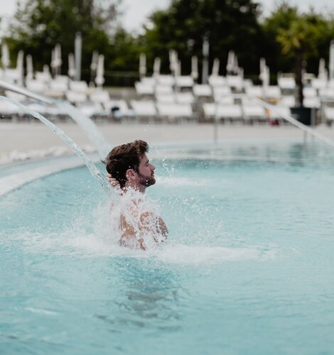 Mann genießt das Wasser unter der Schwalldusche im Thermal-Becken des Spa Resort Geinberg | © Spa Resort Geinberg / Chris Perkles