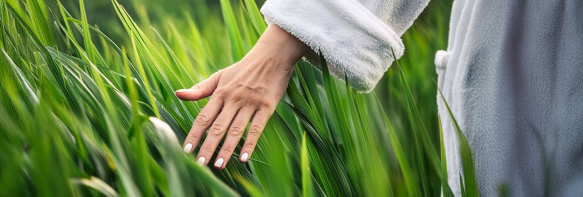 Hand im flauschigen Bademantel in hohem Gras